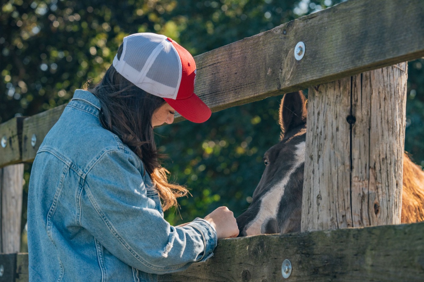 Model in a red trucker cap with a horse at the fence