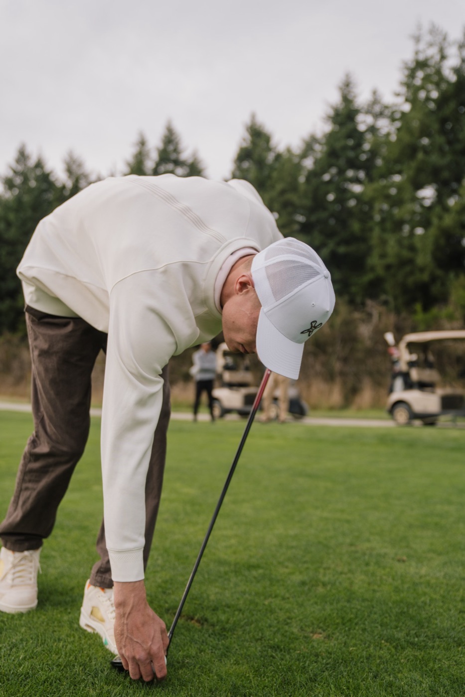 Golfer in a white trucker cap teeing up a ball