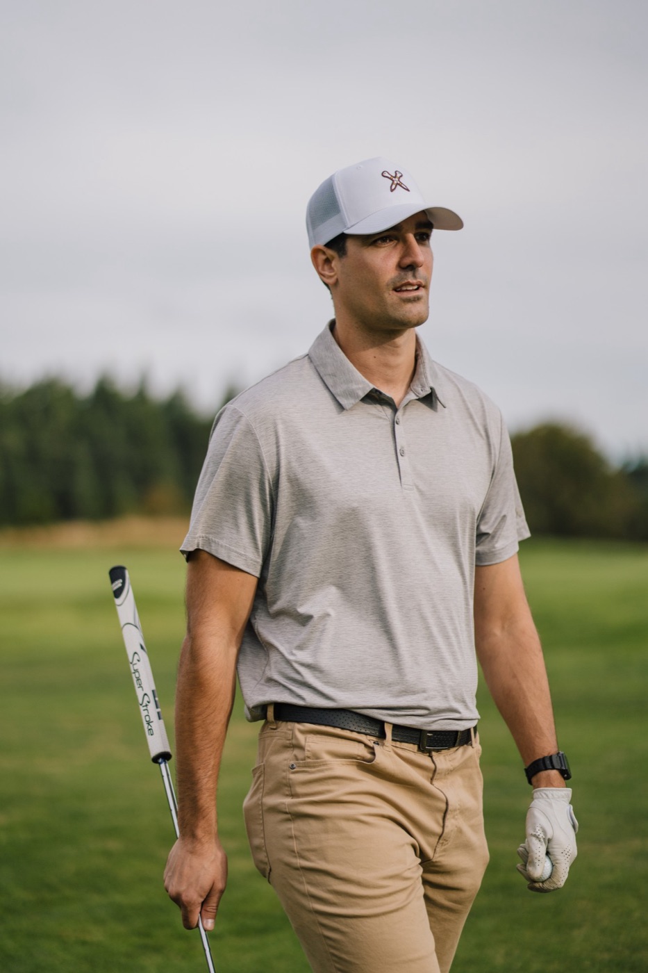 Golfer in a white trucker cap walking the fairway with a putter