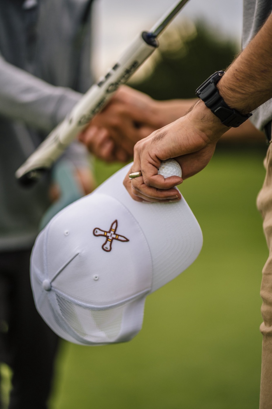 Hand holding a white trucker cap and a golf ball