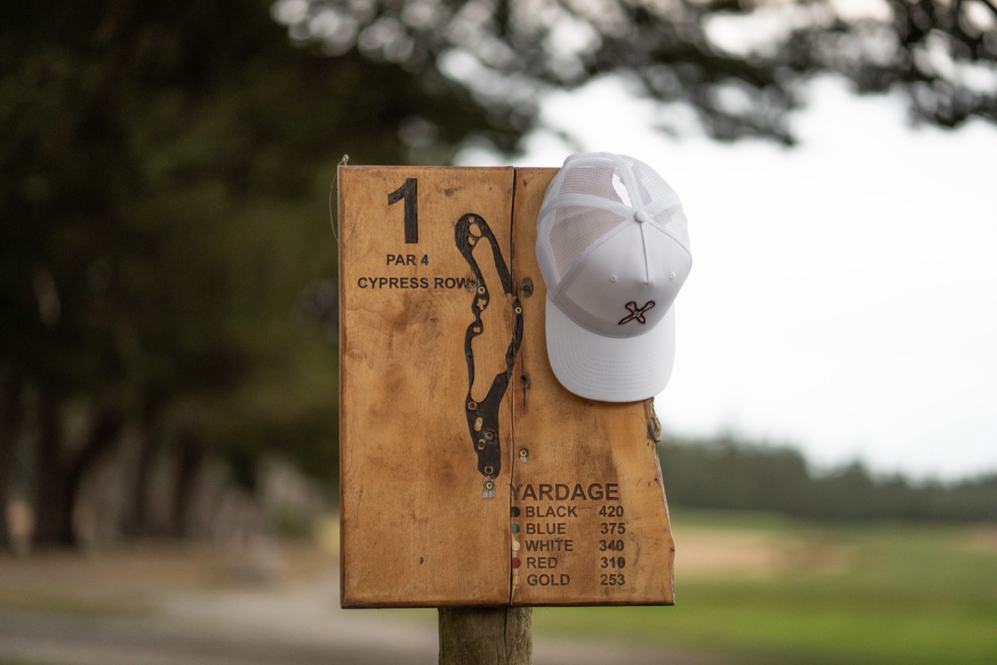 White trucker cap hanging on a wooden first-hole sign