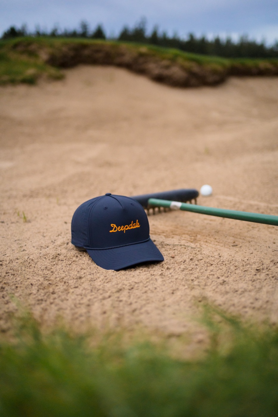 Navy Deepdale cap resting in a sand bunker beside a rake