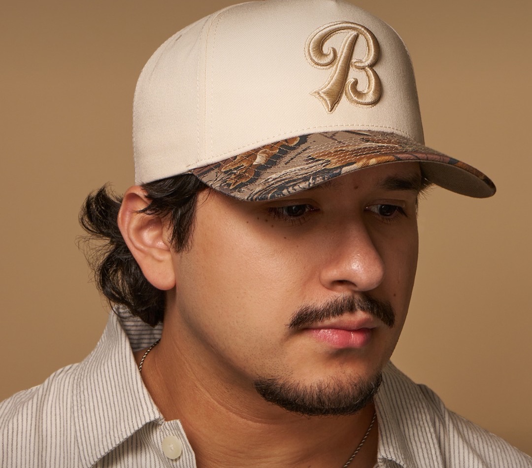 Close-up of a cream cap with a camo brim and embroidered B