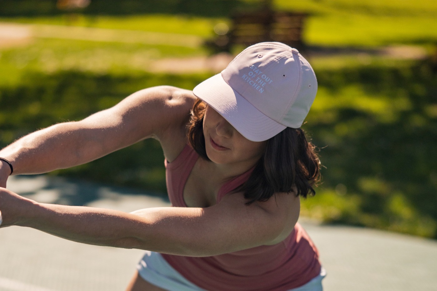 Player mid-swing in a pink Stay Out of the Kitchen cap