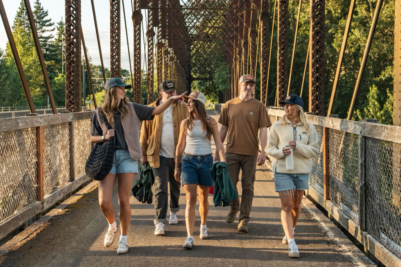 Five friends in trucker caps walking across an old steel bridge
