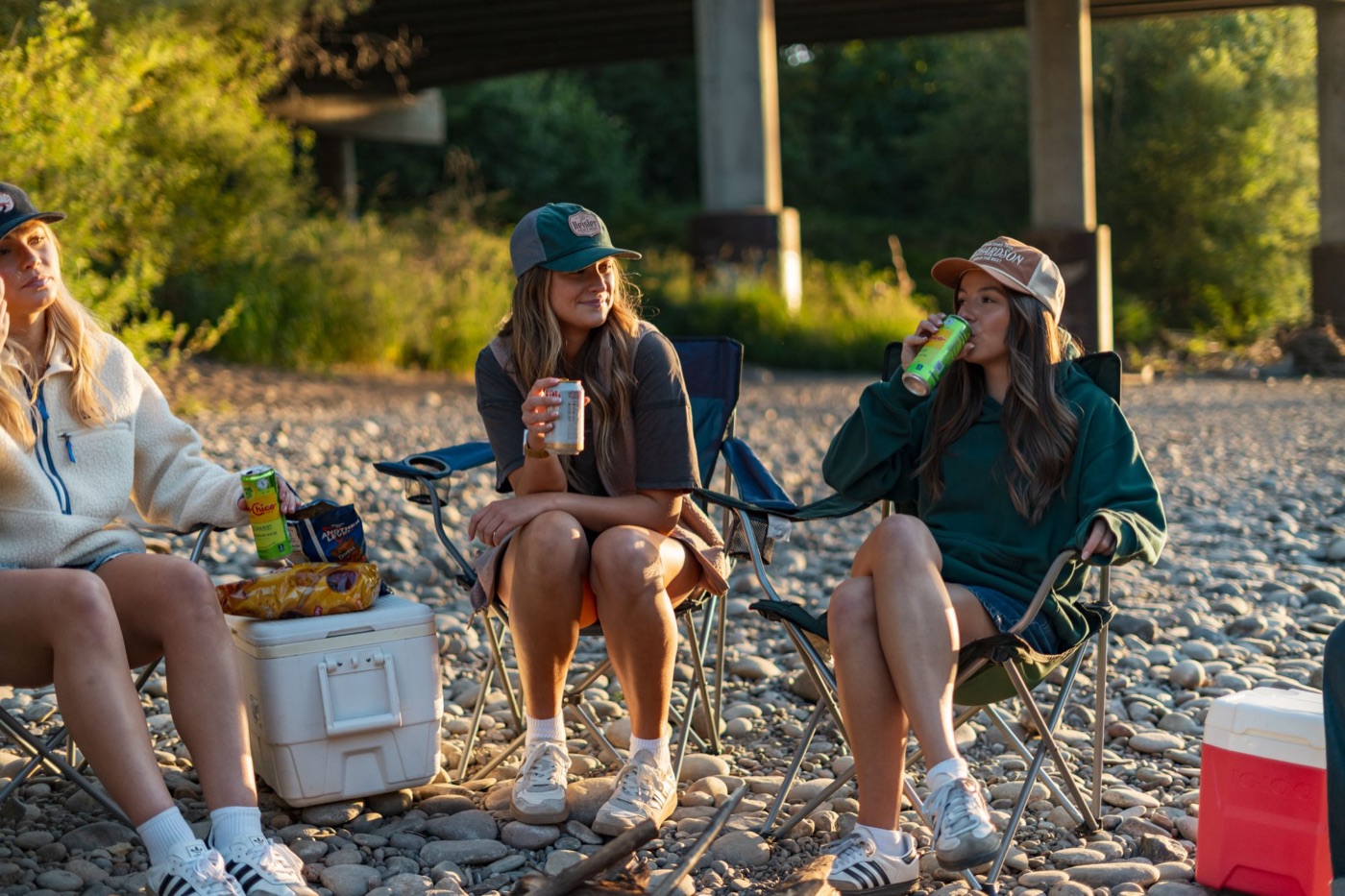 Three friends in camp chairs on the riverbank at sunset