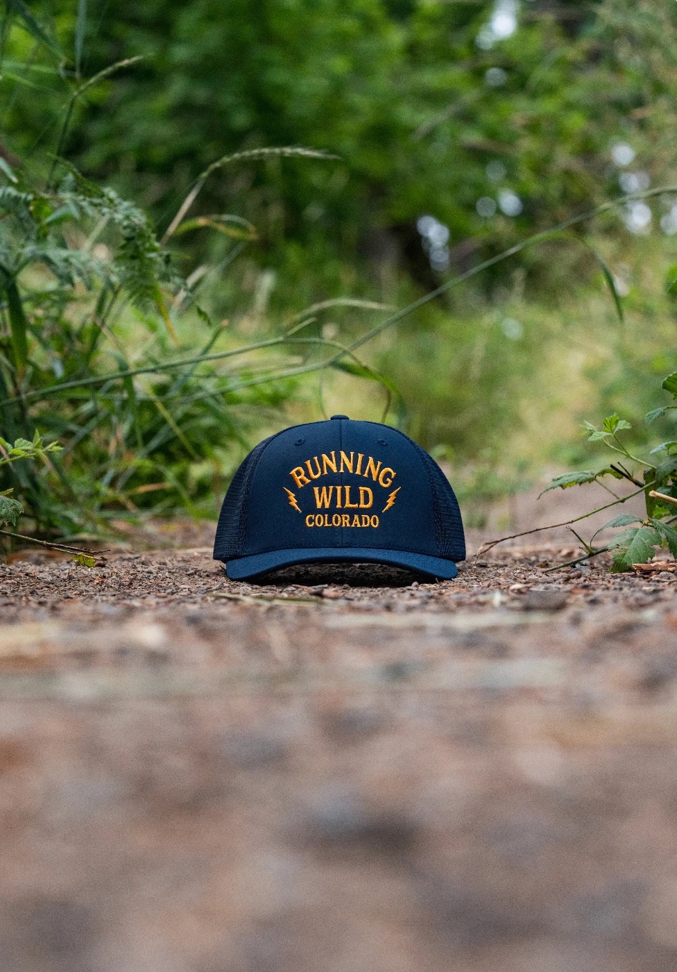Running Wild trucker cap resting on a gravel trail