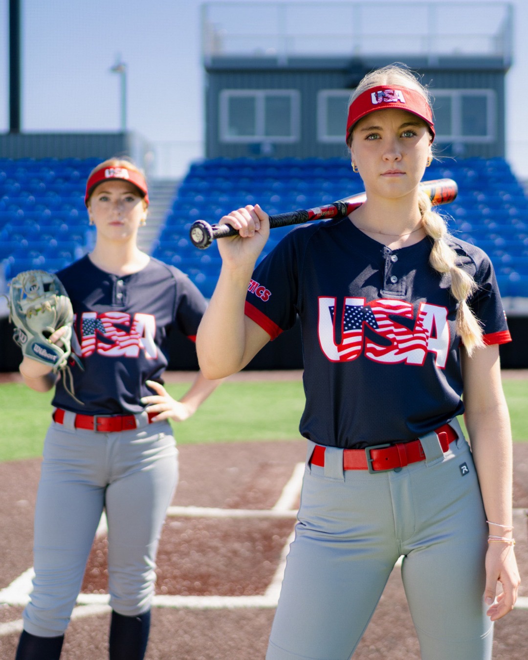 Two USA softball players at home plate with a bat